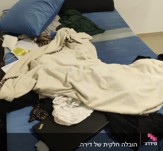 מיטה עם בגדים, מחשב נייד ומטען מפוזרים